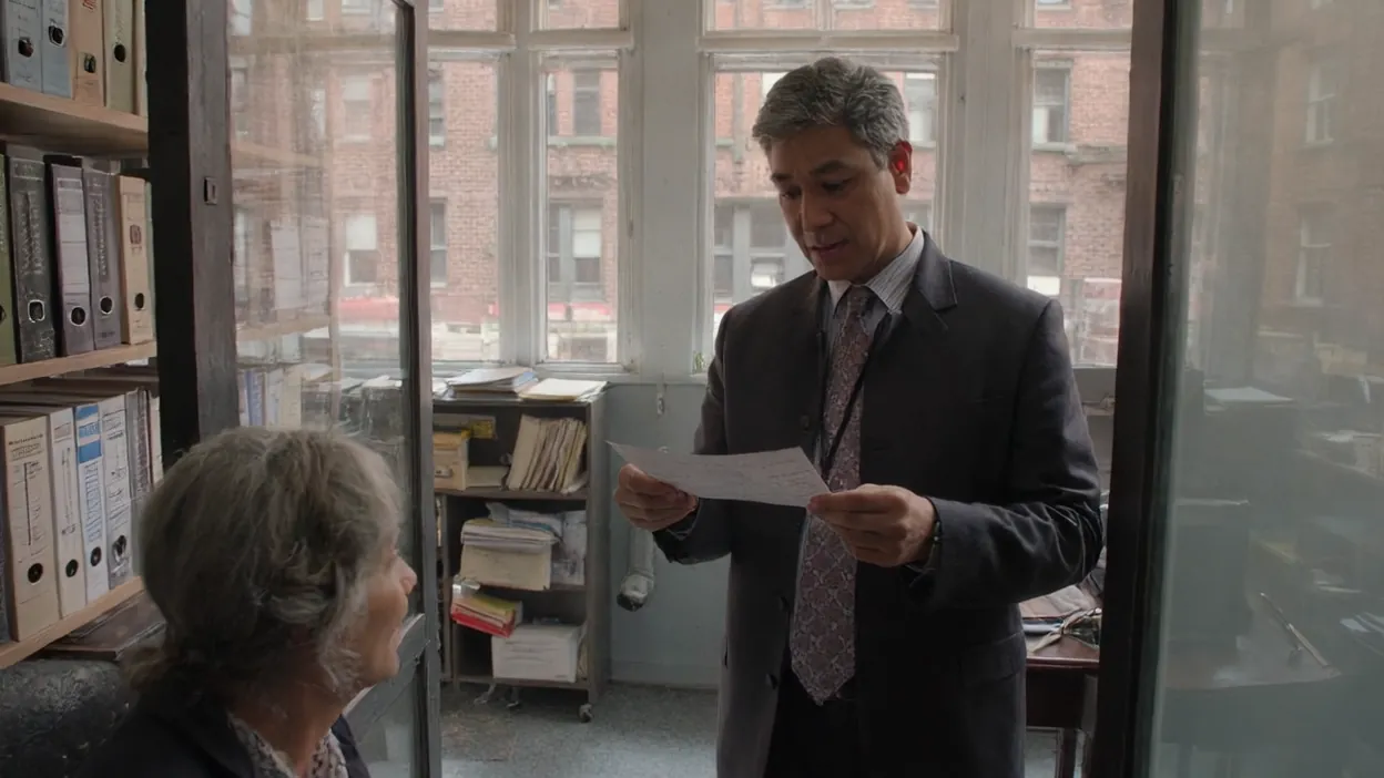 An employee reads a printed request in a doorway as a coworker at her desk looks up at him.