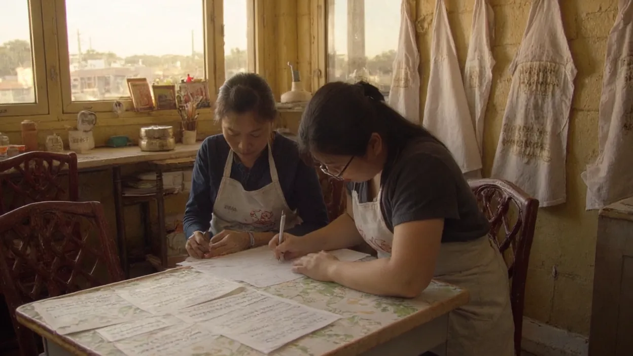 A bakery owner and her office manager fill in a printed sheet together at a table in the shop.